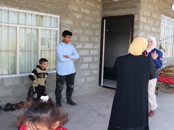 A women wearing an UNMAS jacket is talking to a woman wearing black robe. In a background, there are some children around them. 
