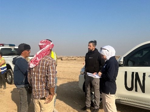 A group of people are standing and talking in front of an UN car in a field.
