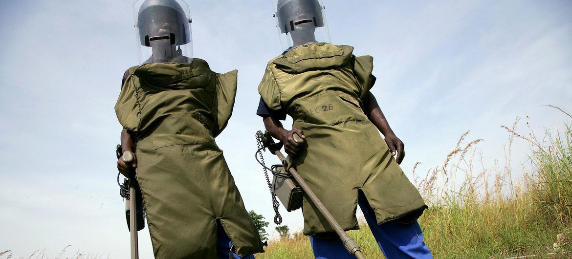 Two deminers wearing protective equipment holding metal detectors