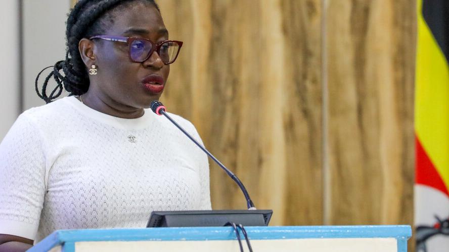 A young woman standing at a podium speaking into a microphone with a flag in the background.