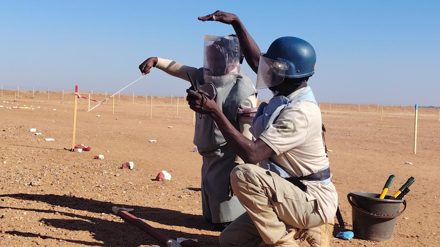 a deminer is receiving training from another deminer in the field