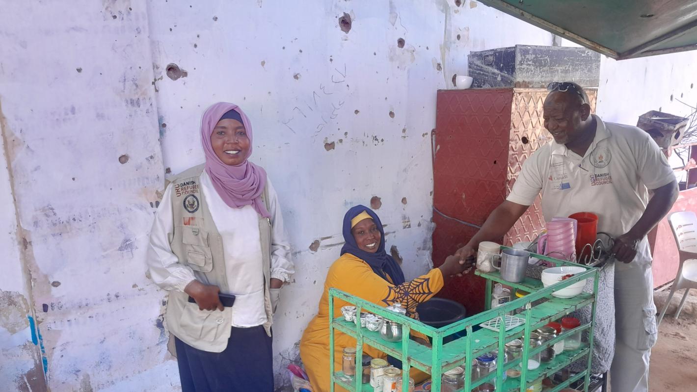 a coffee stand owner is shaking hand to a man with a woman standing beside them
