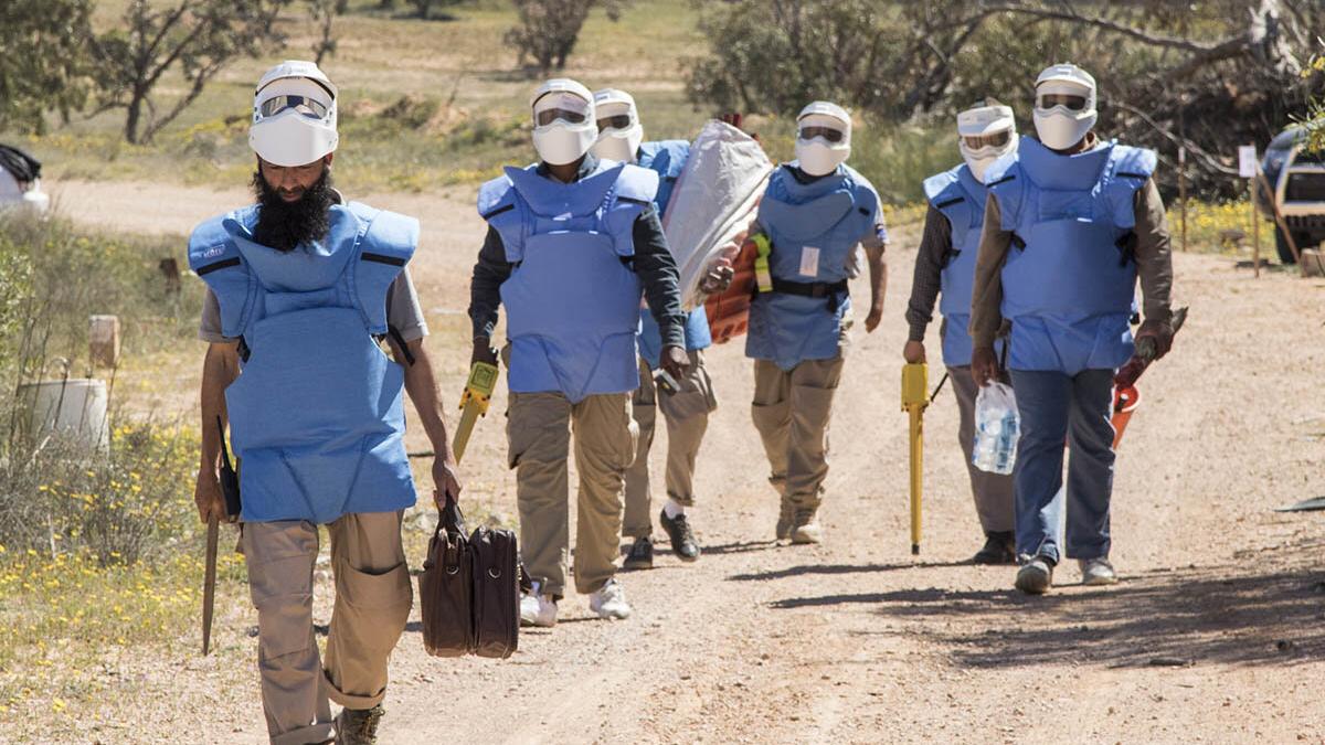 some deminers are walking and holding detectors and equipments.