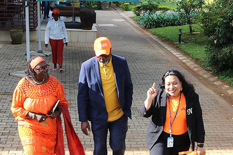 A man and two women walking down a path. All three are wearing orange coloured clothing.
