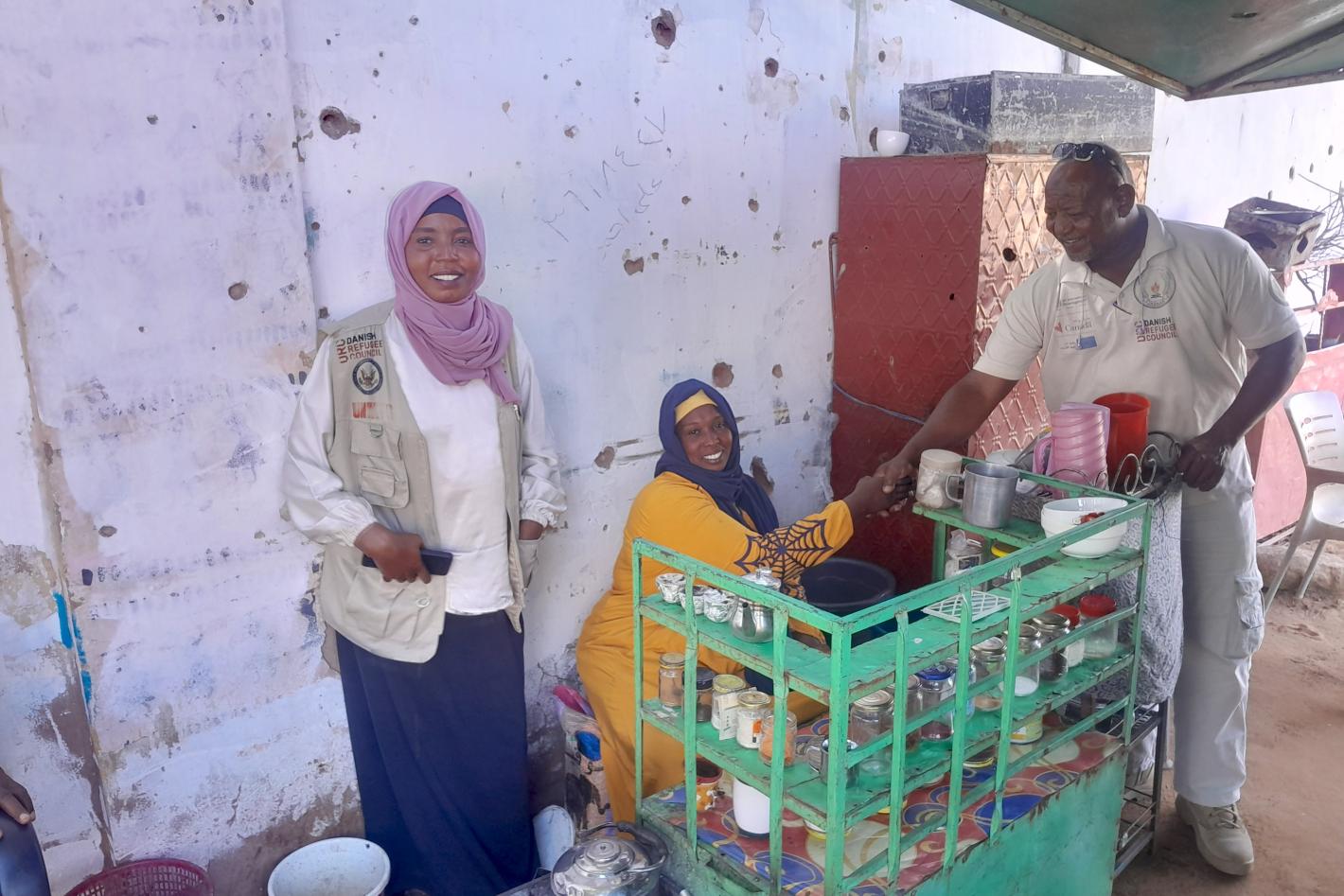 a coffee stand owner is shaking hand to a man with a woman standing beside them