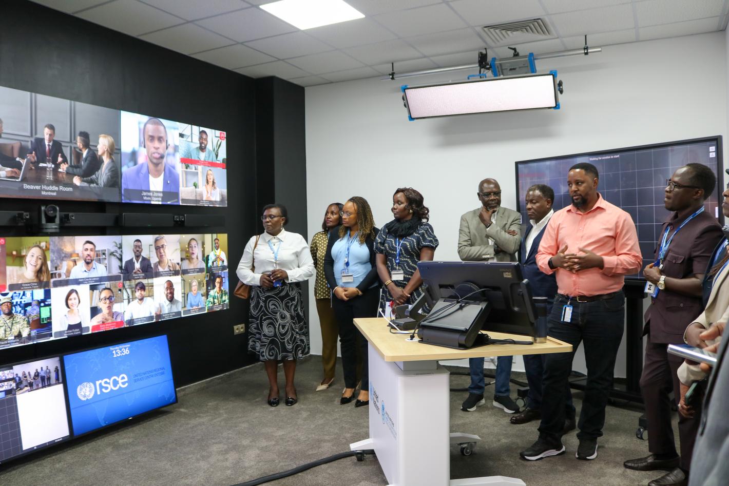 A group of people look at multiple TV screens with video conference calls displaying