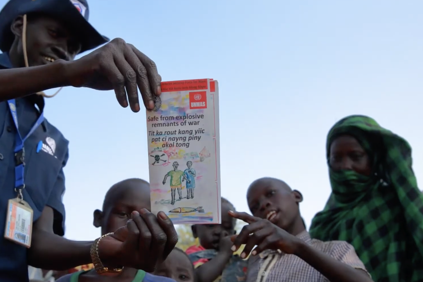 a man in unmas uniform is showing a mine awareness flyer to some kids