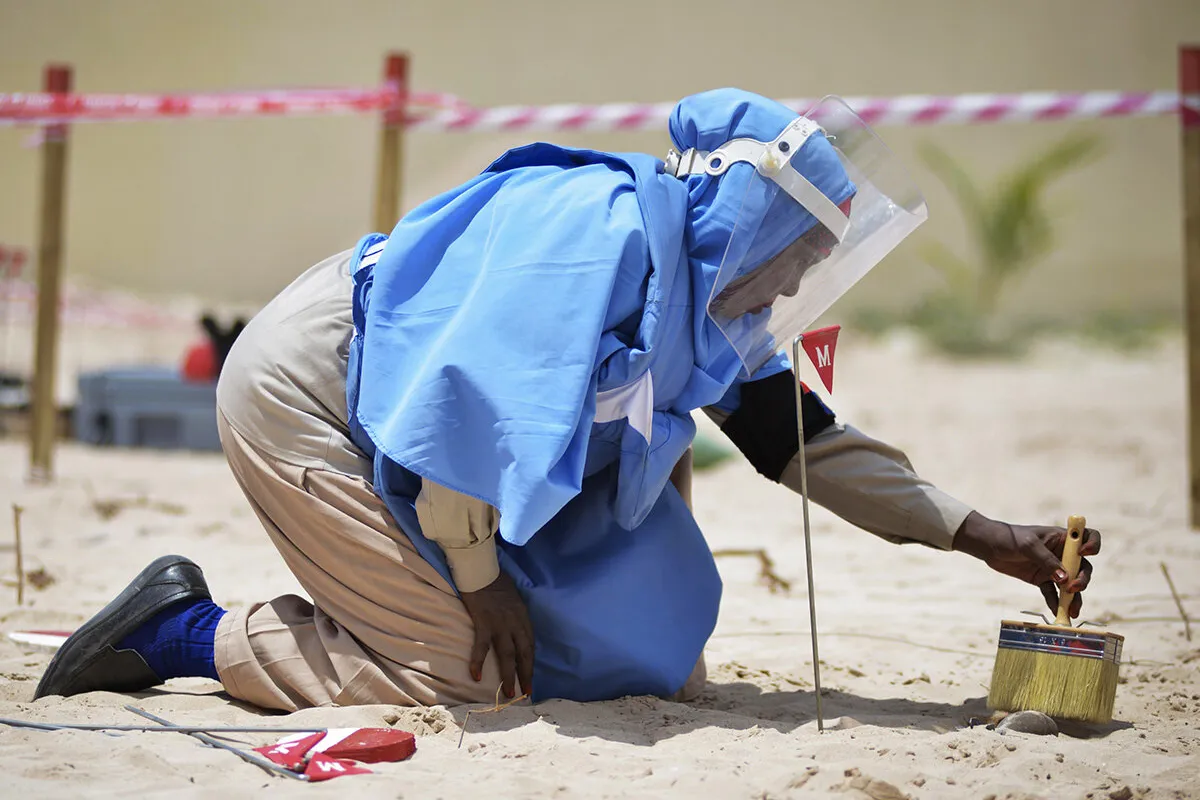 A female member of an Explosive Ordnance Disposal team brushes sand off of a mortar shell during a demonstration held by UNMAS in Mogadishu, Somalia.
