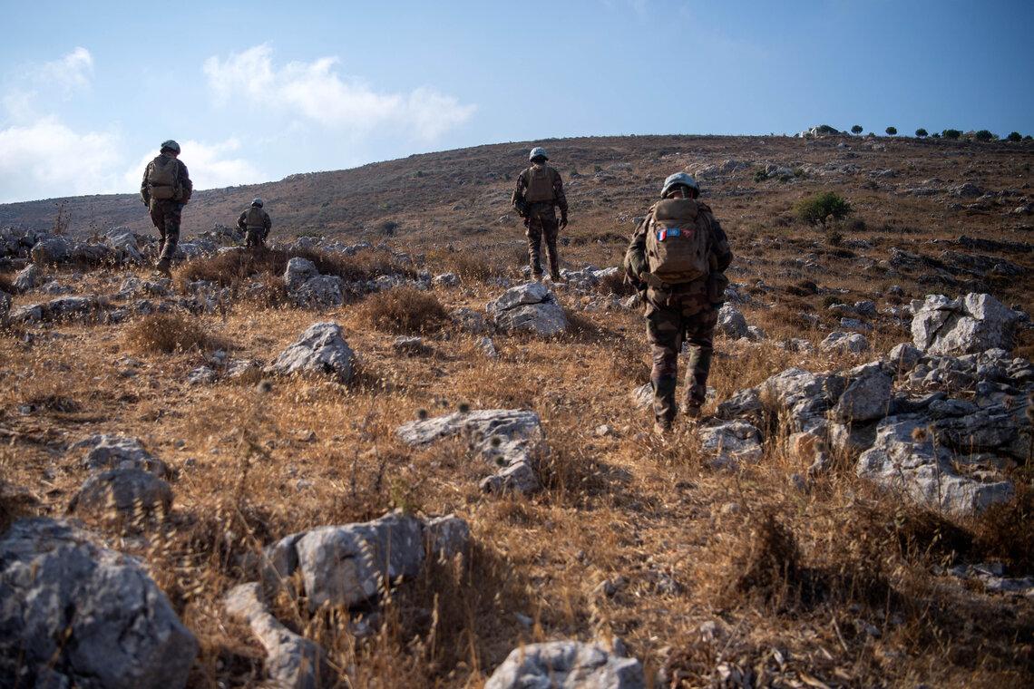 Four UN peacekeepers in blue helmets walk through rolling hills under a blue sky